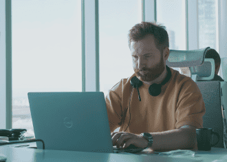 Man concentrating on laptop work at a contemporary office desk, wearing headphones.