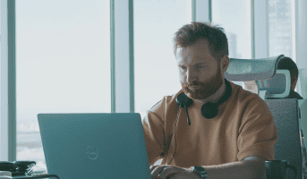 Man concentrating on laptop work at a contemporary office desk, wearing headphones.