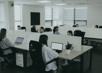 Modern open-plan office showing team members working independently at shared desks with laptop computers.