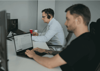 Office team members working on laptops with headsets, focused on computer-based office tasks.