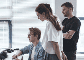 Team members gathered around a desk, debugging a software issue in front of a screen in a naturally lit office