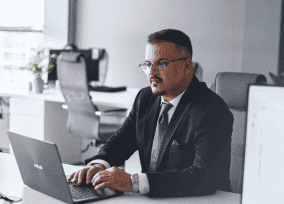 Well-dressed focused developer coding on a laptop at a shared desk in a modern office setting