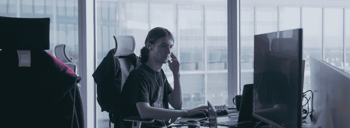 IT expert on a sprint planning video call with clients, wearing earphones and focused on a computer screen in a bright office space