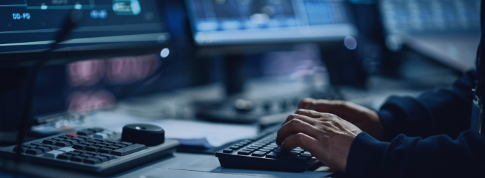 Developer writing code on a keyboard, surrounded by multiple screens with software interfaces