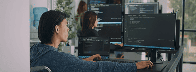 Developer collaborating with team, reviewing code on multiple monitors in a bright office